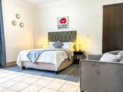 a bedroom with a large bed and a chair at Bobisemo Luxury Pretoria East Apartment in Tierpoort