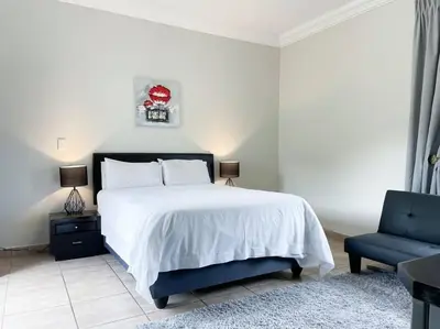 a bedroom with a white bed and a blue chair at Bobisemo Luxury Pretoria East Apartment in Tierpoort