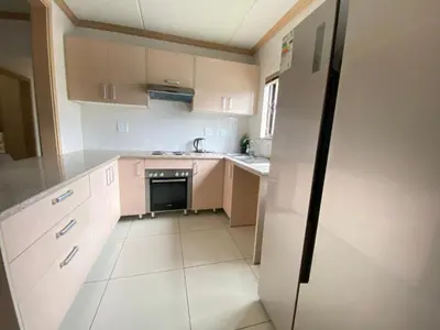 a small kitchen with white cabinets and a refrigerator at Siena Sun Apartment 10 in Midrand