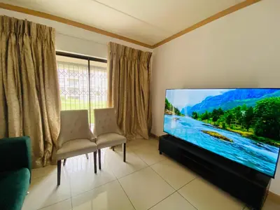 a living room with a flat screen tv and two chairs at Siena Sun Apartment 10 in Midrand