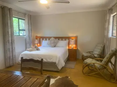 a bedroom with a large bed and a chair at Vlakkieskraal FarmStay - Bosvark Cabin in Bela-Bela