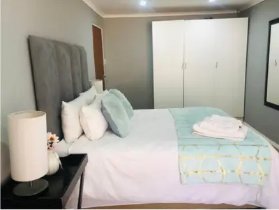 a bedroom with a white bed with pillows and a lamp at Serenity Cottage in Benoni