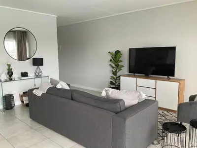 a living room with a gray couch and a flat screen tv at The Blyde Stylish Homes in Pretoria