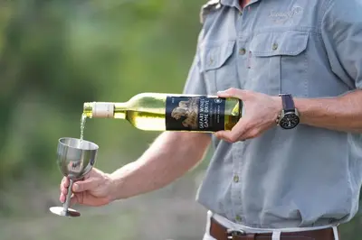 a man pouring a bottle of wine into a glass at Sausage Tree Safari Camp in Balule Game Reserve