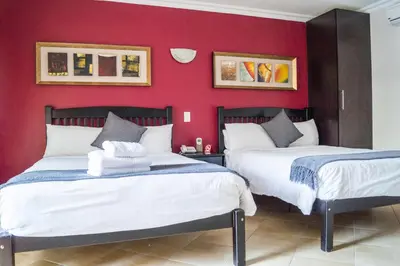 two beds in a room with red walls at Ivory Lodge Bendor in Polokwane