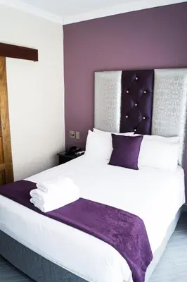 a bedroom with a large white bed with a purple headboard at Ivory Lodge Bendor in Polokwane