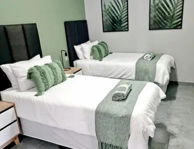 two beds in a room with green and white at Wild Fig Rest Guest House in Polokwane