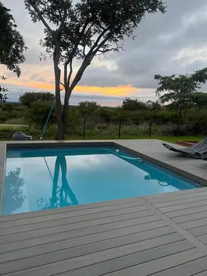 a blue swimming pool with a tree in the background at De Marea villa in Naboomspruit