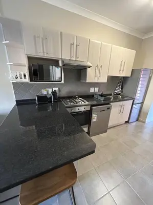 a kitchen with white cabinets and a black counter top at Home away from Home in Pretoria