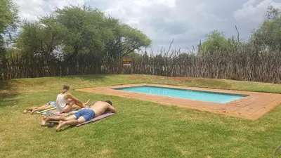 a group of people laying on the grass by a swimming pool at Makhato 84 Bush Lodge in Bela-Bela