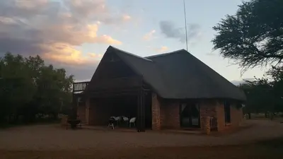a brick building with a black roof with white chairs at Makhato 84 Bush Lodge in Bela-Bela