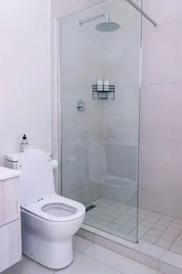 a white bathroom with a shower and a toilet at Luminant Escapes -With Power Backup in Midrand