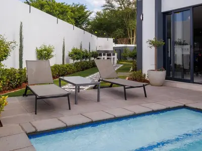 two chairs and a table next to a swimming pool at Luminant Escapes -With Power Backup in Midrand