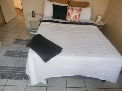a large white bed with black pillows on it at Apartment@VillaVel in Midrand