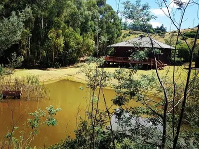 a hut next to a body of water with trees at Incwala Lodge in Waterval Boven