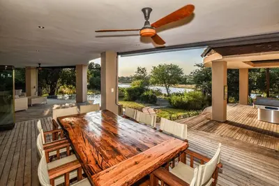 a wooden table and chairs on a deck with a ceiling fan at Impangele River Lodge in Hectorspruit