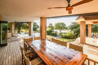 a dining room with a wooden table on a deck at Impangele River Lodge in Hectorspruit