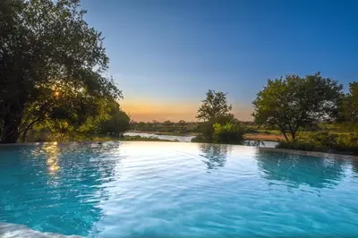 a large pool of blue water with trees in the background at Impangele River Lodge in Hectorspruit