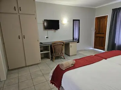 a bedroom with a bed and a desk with a television at Pietersburg Lodge in Polokwane