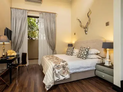 a bedroom with a bed and a desk and a window at Buffelshuis Safari Camp in Golders Green