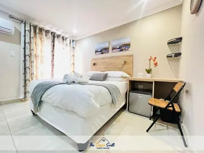 a white bedroom with a large bed and a desk at The Curve Suite Guest House in Nkowakowa