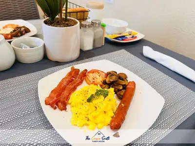 a plate of food with sausage and eggs on a table at The Curve Suite Guest House in Nkowakowa