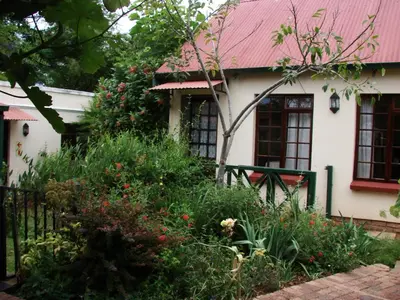 a white house with a red roof and some plants at Petal Faire Cottage in Pretoria