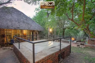 a building with a thatch roof and a bed at Nag-Apie Vakansiehuis in Marloth Park