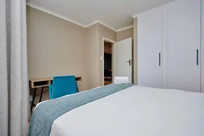a bedroom with a bed and a desk with a blue chair at Unit 404 at Menlyn Place in Pretoria