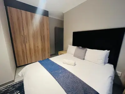 a bedroom with a large bed and a wooden cabinet at Spacious 2 Bedroom Apartment in Midrand, Waterfall City - Business and Family friendly - 11 Elizabeth Place in Midrand