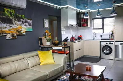 a living room with a couch and a kitchen at Air-Conditioned, Self-Catering Apartment with Heated Pool Near OR Tambo International Airport in Benoni