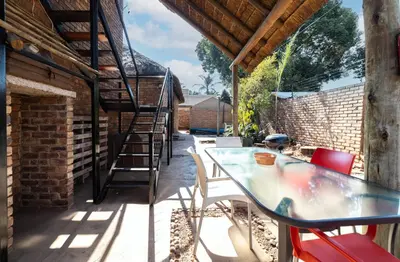 a patio with a table and chairs and a ladder at Thatch Haven Guesthouse in Centurion
