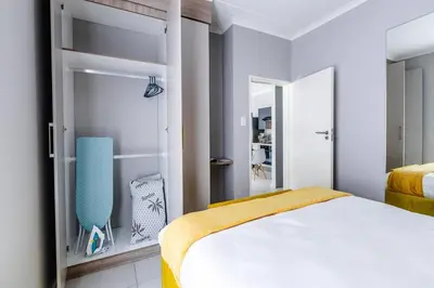 a white bedroom with a bed and a blue chair at Central Serenity @Midrand in Midrand