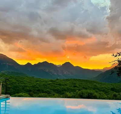 a swimming pool with a view of mountains at sunset at umVangati House in Hoedspruit