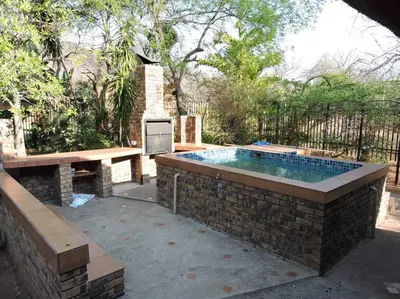 a swimming pool in a brick wall with a table and a bench at Collin's Rest in Marloth Park