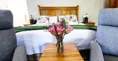a vase of flowers on a table in front of a bed at Tswenyane Kruger Lodge in Marloth Park