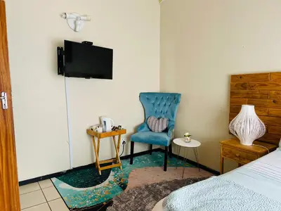 a bedroom with a blue chair and a tv at Wampi guesthouse in Polokwane