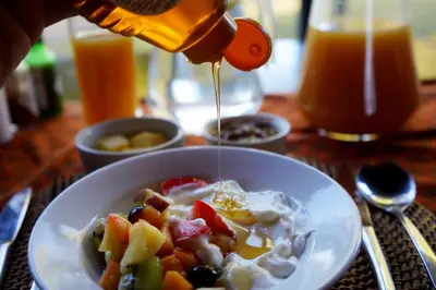 a person is pouring cereal into a bowl of fruit at Mapesu Wilderness Tented Camp in Musina