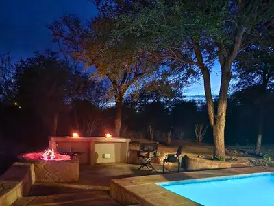 a backyard with a swimming pool and a fire pit at night at Stella Bush Villa in Hoedspruit