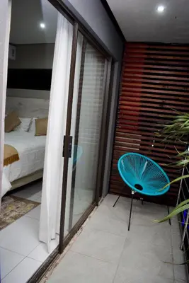 a room with a bed and a blue chair on a balcony at De Guest @115 in Centurion