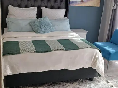 a bed with a green and white blanket and a blue chair at Serene B&B in Midrand