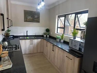 a kitchen with wooden cabinets and black counter tops at EDJAMI Guest House in Marloth Park