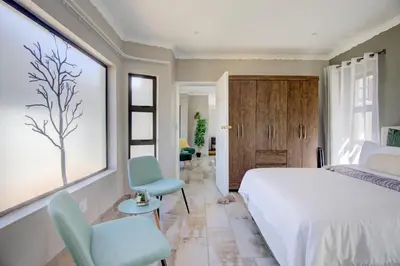 a bedroom with a white bed and two blue chairs at Kirrin Cottage in Benoni in Benoni