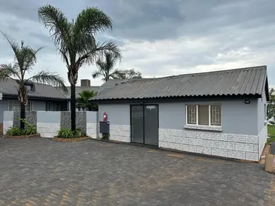 a white house with a black door and a palm tree at Eagles View Kungwini in Erasmus
