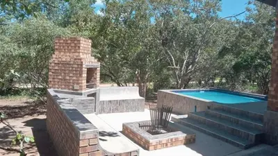 a backyard with a brick fireplace and a swimming pool at Woodlands on Korhaan 2926 in Marloth Park