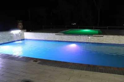 a large swimming pool at night with a fountain at Falcon Lodge (ET) in Bela-Bela