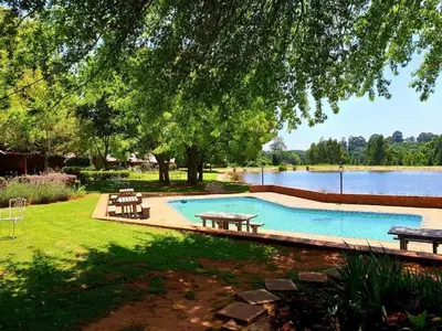 a swimming pool with picnic tables and a lake at Critchley Hackle Lodge in Dullstroom
