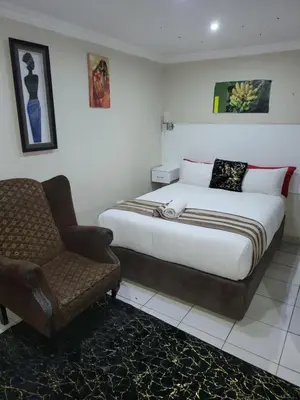 a bedroom with a bed and a chair in it at Tshedza Guest House in Pretoria
