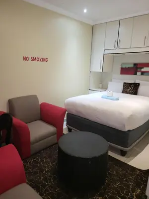 a room with a bed and a couch and a chair at Tshedza Guest House in Pretoria