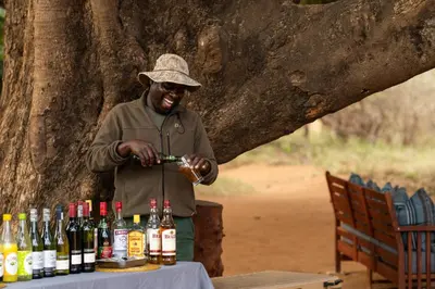a man standing next to a table with bottles of alcohol at Hutwini Walking Camp by RETURN Africa in Makuleke Contract Park